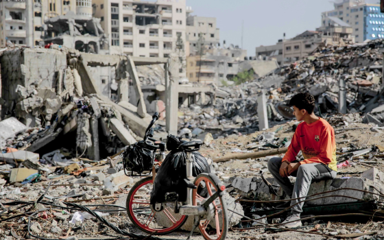 فتى من غزة يجلس بين آثار الدمار الذي أحاط بالمباني في غزة