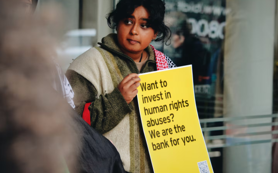 فتاة تحمل لافتة منددة باستثمار البنك في شركة داعمة للمستوطنات