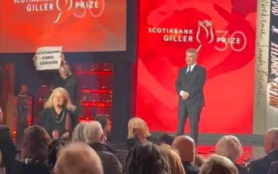 شخص يرفع لافتة منددة بشراكة جائزة جيلر مع سكوتيا بنك الممول للإبادة- أحد إحتفاليات جيلر