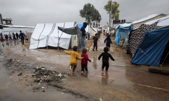 أطفال يركضون أمام خيم النزوح المحاصرة بالأمطار